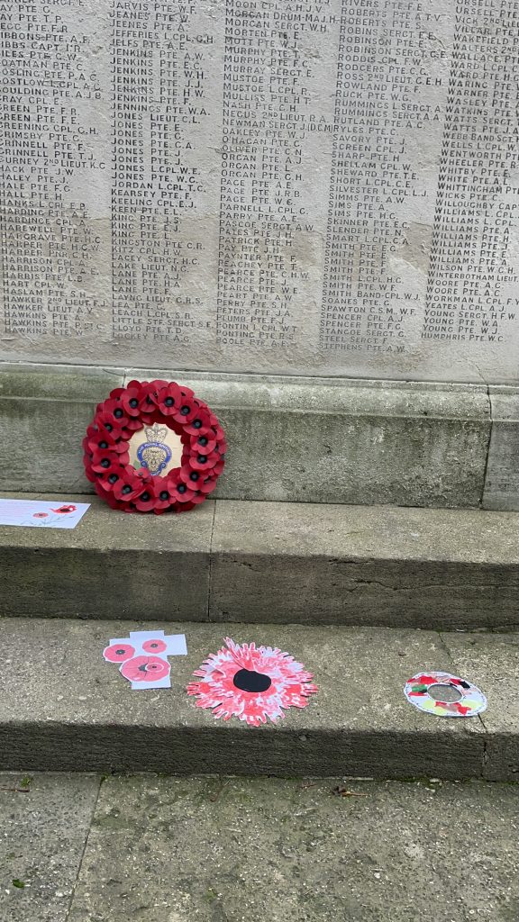 A close up image of the war memorial statue. There are thousands of names engraved on the stone. There are wreathes made of red poppies placed on the ground around it. The stone is grey and a bit mouldy.